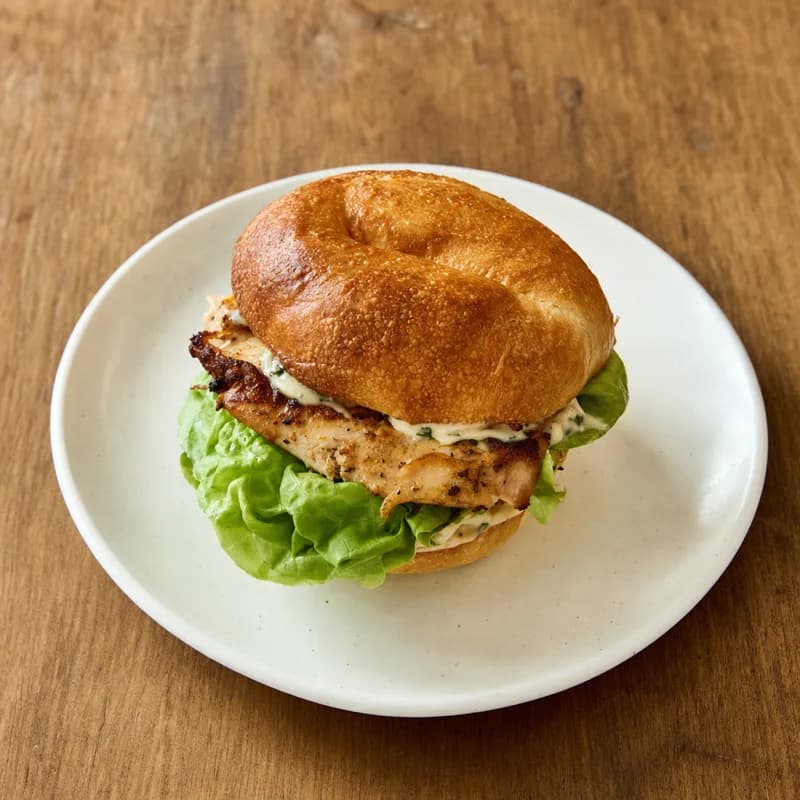 A chicken sandwich on a toasted roll, plated on a white dish